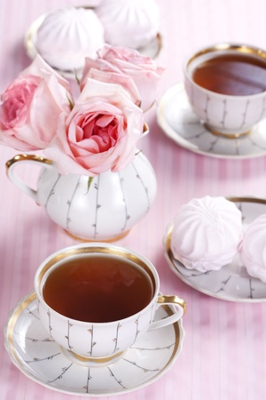 Two cups of tea, sweets and a bouquet of roses on a pink backgroundの写真素材