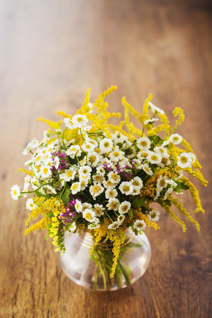 Wildflowers bouquet in glass vase on wooden backgroundの写真素材