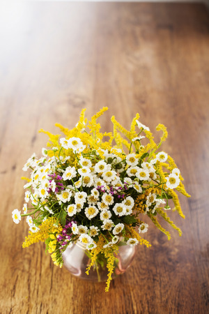Wildflowers bouquet in glass vase on wooden backgroundの写真素材
