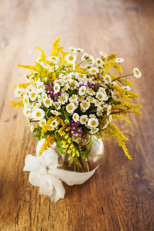 Wildflowers bouquet in glass vase on wooden backgroundの写真素材