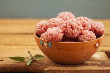 Raw meatballs in bowl with ingredients on wooden backgroundの写真素材