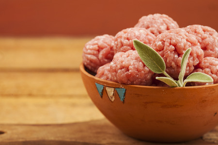 Raw meatballs in bowl with ingredients on wooden backgroundの写真素材