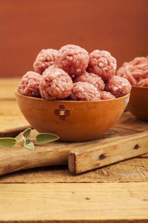 Raw meatballs in bowl with ingredients on wooden backgroundの写真素材