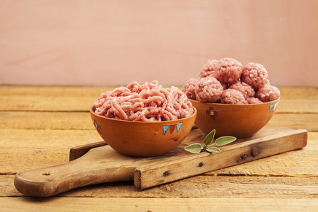 Raw meatballs in bowl with ingredients on wooden backgroundの写真素材