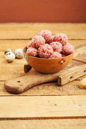 Raw meatballs in bowl with ingredients on wooden backgroundの写真素材