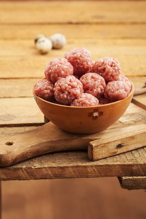 Raw meatballs in bowl with ingredients on wooden backgroundの写真素材