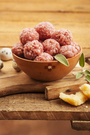 Raw meatballs in bowl with ingredients on wooden backgroundの写真素材