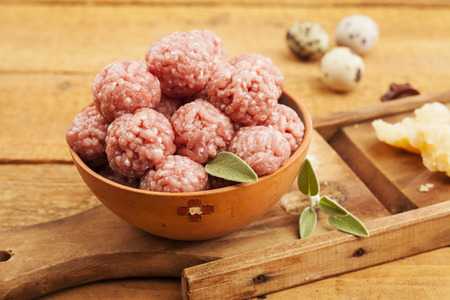 Raw meatballs in bowl with ingredients on wooden backgroundの写真素材