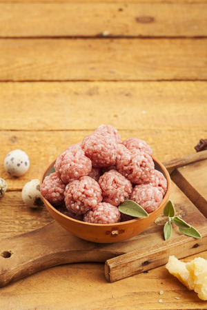 Raw meatballs in bowl with ingredients on wooden backgroundの写真素材