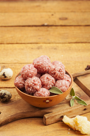 Raw meatballs in bowl with ingredients on wooden backgroundの写真素材