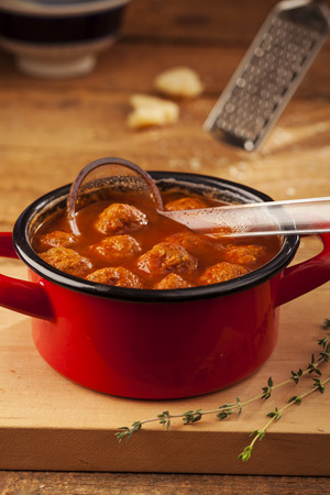 Meatballs closeup in a red casserole on wooden backgroundの写真素材