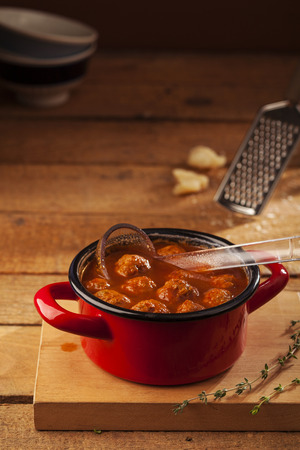 Meatballs closeup in a red casserole on wooden backgroundの写真素材