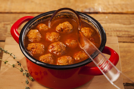 Meatballs closeup in a red casserole on wooden backgroundの写真素材