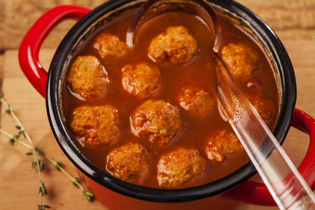 Meatballs closeup in a red casserole on wooden backgroundの写真素材