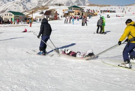 Two members of a ski patrol helping an injured skier down the mountainのeditorial素材