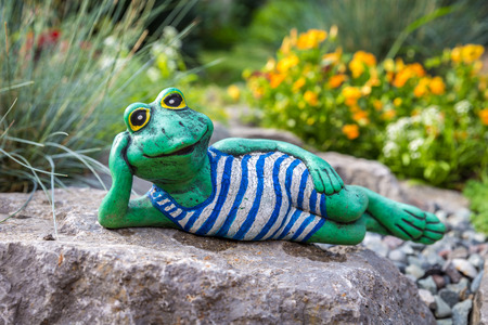 Garden frog lying among beautiful flowers, artificial toyの写真素材