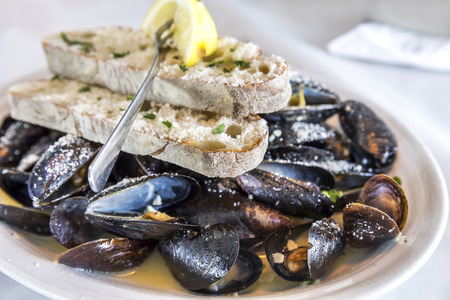 Plate of steamed mussels in sauce with bread, cheese and lemon