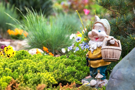 Funny garden gnome standing among nice flowersの写真素材