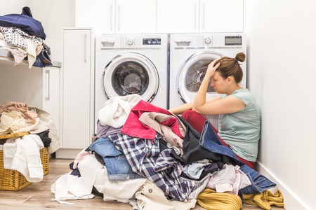 Sad woman sitting in a laundry roomの写真素材