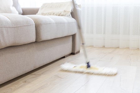 Cleaning floor with white mop near sofa