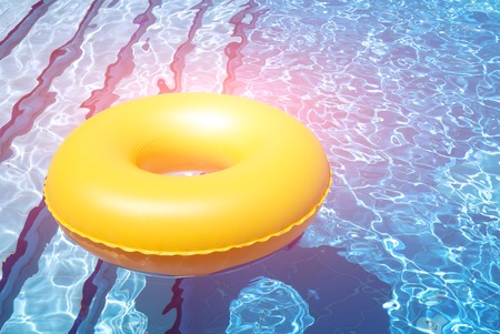 inflatable yellow inner tube floating in clear blue waters in pool with bright lightの写真素材
