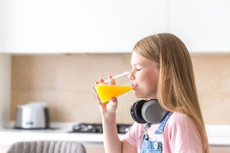 Girl with headphones drinking orange juice in the kitchenの写真素材