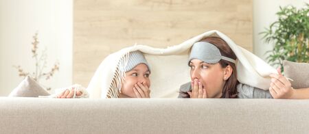 Mother and daughter wearing sleeping mask having fun on couch with copy space