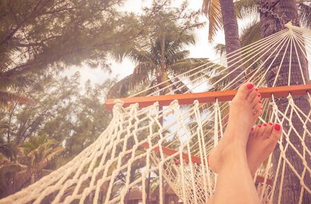 Woman Feet in a hammock with palm trees and bright sunset. Vacation concept with orange color toneの写真素材