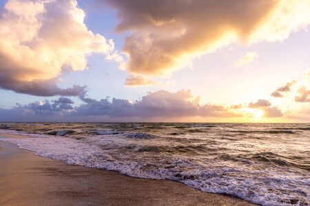 Beautiful cloud coastline background. Fiery orange sunset sky. Amazing sunrise on the beach in...