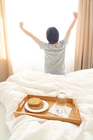 Tray with water and crackers breakfast on a bed with woman stretching on backgroundの写真素材