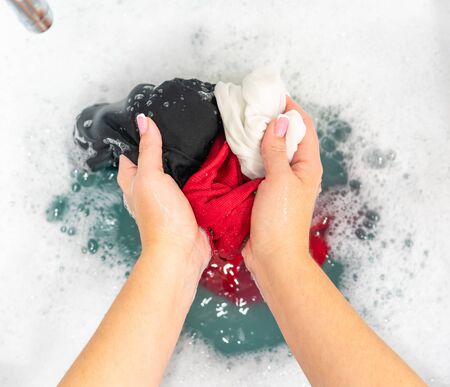 Red, black and white clothes in basin with detergent foamの写真素材