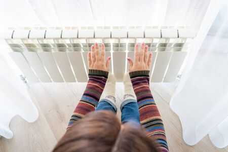 Girl warms up the frozen hands above hot radiator, close up view