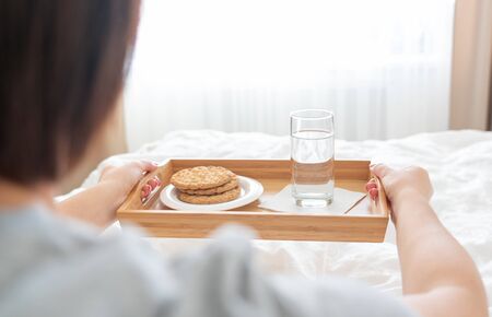 Woman holding tray with diet breakfast of crackers and water on a bedの写真素材