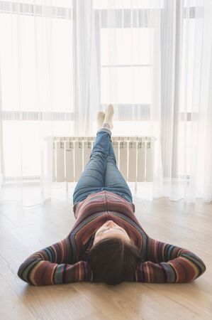 Woman laying on floor with feet raised up on radiator for warming upの写真素材