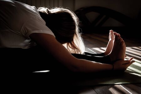 Young woman stretching in yoga pose on mat, silhouette in darkの写真素材