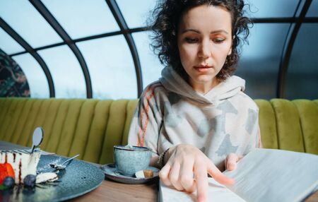 young business woman sitting in cafe at table and planning working schedule and recording to notepad