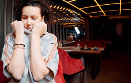 Sad girl with closed eyes standingnear table in cafe upsetの写真素材