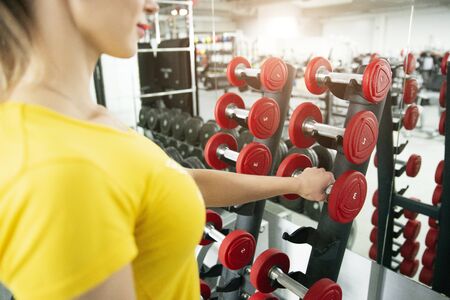 Woman taking dumbbells in the fitness gym with dumbbells on rackの写真素材