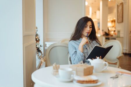 Thoughtful young woman holding notepad and thinking on creative ideas for writing essayの写真素材