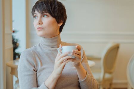 Portrait of young pretty woman with short hair drinking coffee in cafeの写真素材