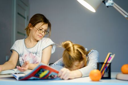 Mother helping her tired daughter with homework at home.の写真素材