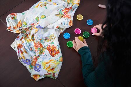 close-up hands of woman seamstress tailor ( dressmaker) designer wedding dress sews beads to lace on...