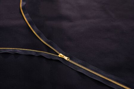 Open golden zipper on black fabric