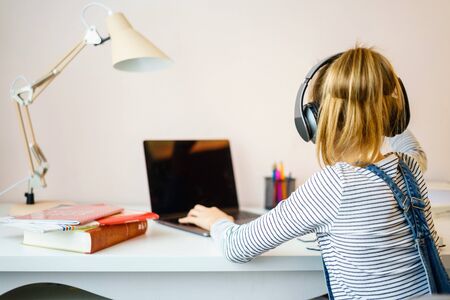Portrait of a student learning on line with headphones and laptop taking notes in a notebook sitting...