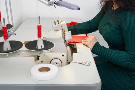 Young tailor using professional overlock sewing machine in workshop studio. Equipment for edging,...