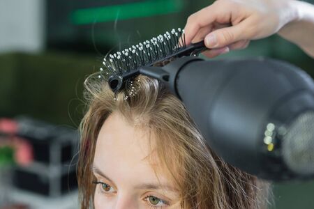 Close up of hairdressers hands drying long blond hair with blow dryer and round brush