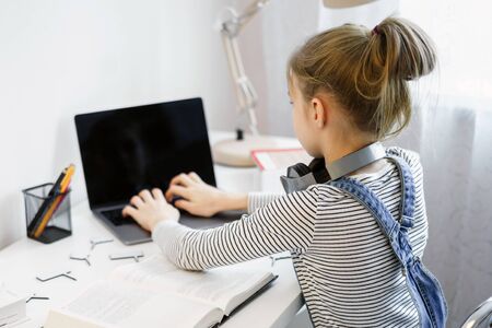 Little girl doing her homework at home and using a laptop