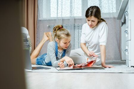 Mother and daughter reading book on the floor at home in the living room
