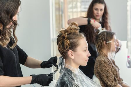 Hairdresser coloring young woman hair using foil