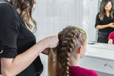 Hairdresser weaves a braid to a preteen blond girlの写真素材
